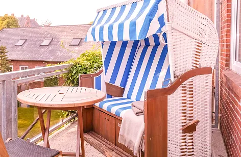Outdoor balcony with blue‑and‑white striped seating, a wicker chair, and a round table under a canopy.