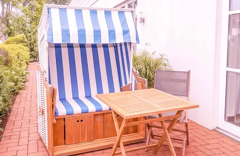 Woman relaxing in a blue-and-white striped outdoor cabana with a wooden table on a brick patio ground