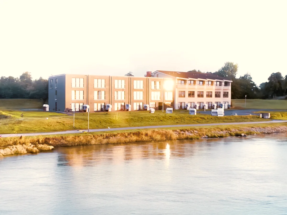 Das Hotel be natural in Tönning mit Strandkörben, gesehen über das Wasser der Eider